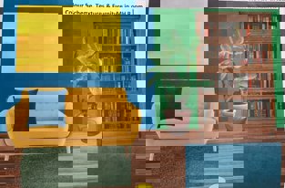 A design of a room with a yellow couch, blue cushion, a plant, a bookshelf and blue, yellow and green wallpaper